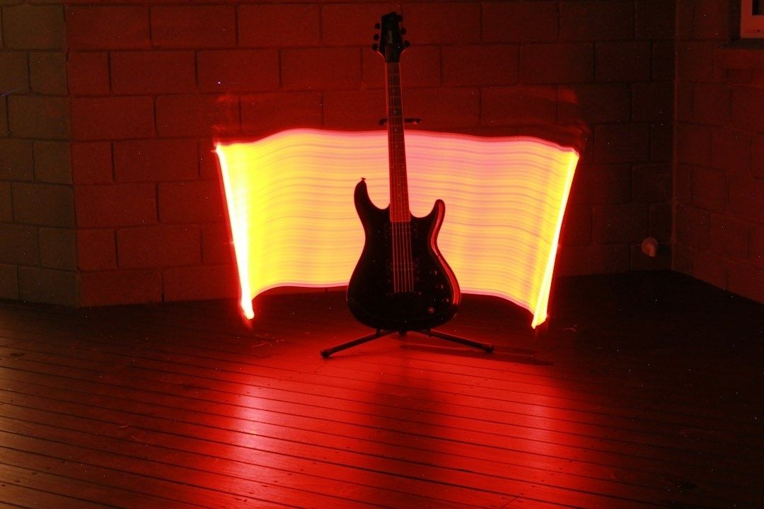 Schwarze E-Gitarre vor rot-gelb leuchtendem Verstärker im dunklen Studio